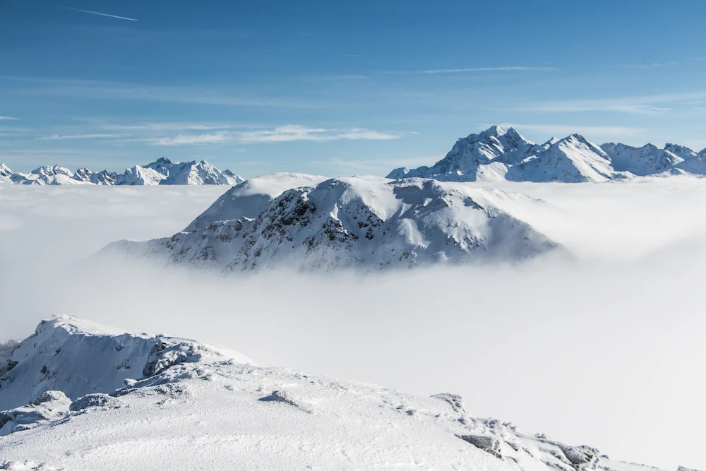 Snow covered mountain tops with clouds below them